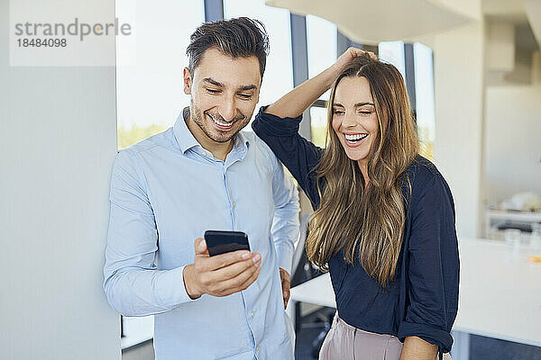 Zufriedene Geschäftskollegen schauen sich ihr Smartphone an und genießen es am Arbeitsplatz