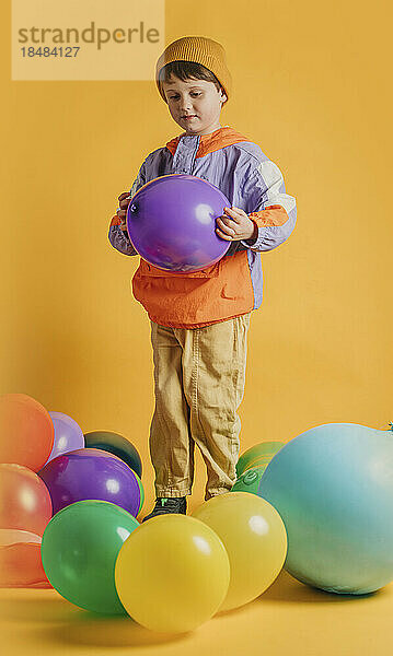Junge spielt mit bunten Luftballons vor gelbem Hintergrund
