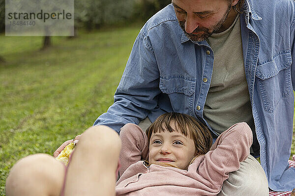 Lächelndes Mädchen entspannt sich mit Vater  der auf dem Feld sitzt
