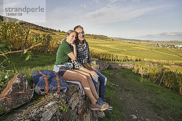 Lächelndes  nachdenkliches Paar sitzt an der Wand im Weinberg