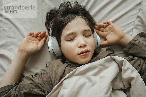 Boy wearing wireless headphones lying on bed at home