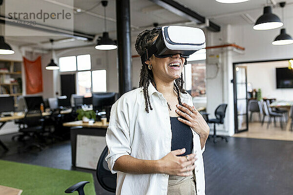 Glückliche Geschäftsfrau mit VR-Brille steht im Büro