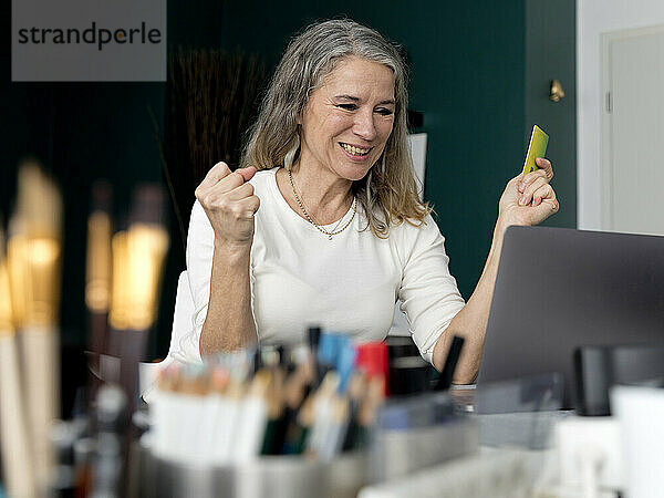 Happy businesswoman holding credit card cheering in office