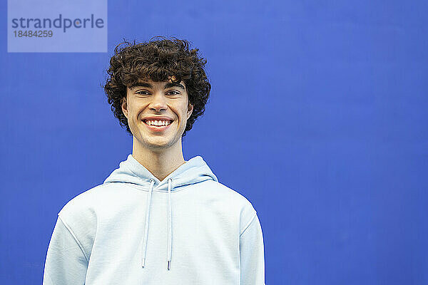 Smiling young man standing in front of blue wall