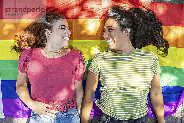 Happy lesbian couple lying down on rainbow colored flag