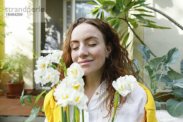 Lächelnde Frau mit geschlossenen Augen hält Narzissenblüten im Hinterhof