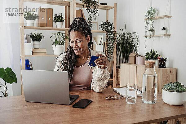 Lächelnder Freiberufler  der im Heimbüro mit Kreditkarte am Laptop bezahlt