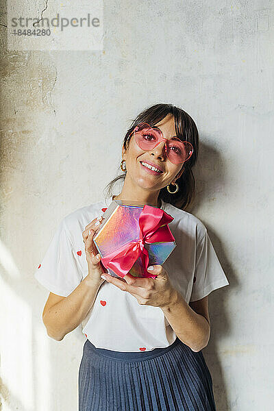 Lächelnde Frau mit Brille steht mit Geschenkbox