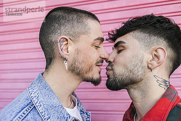 Gay man kissing boyfriend in front of roller shutter wall
