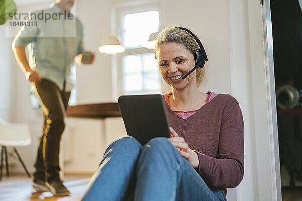 Glücklicher Freiberufler mit Headset  der im Heimbüro am Tablet-PC arbeitet