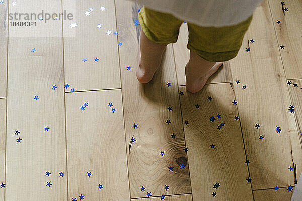 Boy standing on hardwood flooring with star shaped confetti
