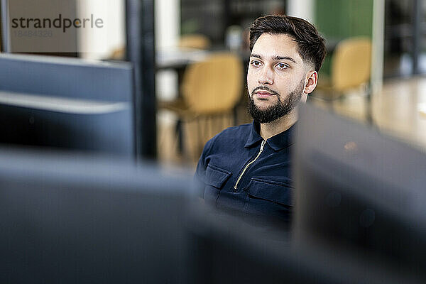 Nachdenklicher junger Geschäftsmann sitzt am Desktop-PC im Büro