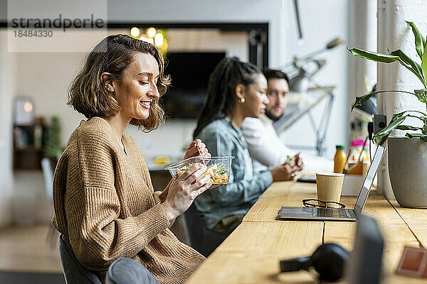 Lächelnde Geschäftsfrau  die in der Mittagspause im Büro Salat isst