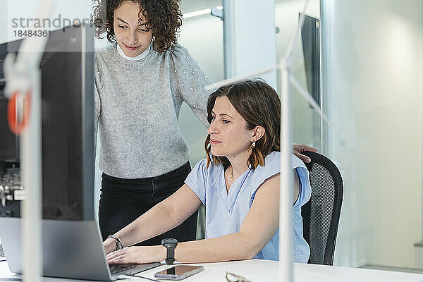 Geschäftsfrau diskutiert mit Kollegin über Laptop am Schreibtisch im Büro