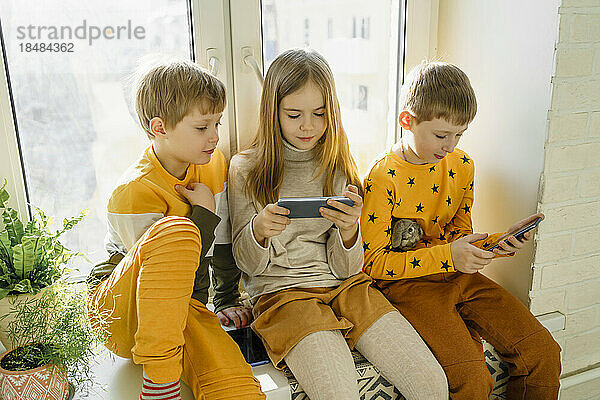 Glücklicher Junge mit Geschwistern  die zu Hause ihr Smartphone nutzen