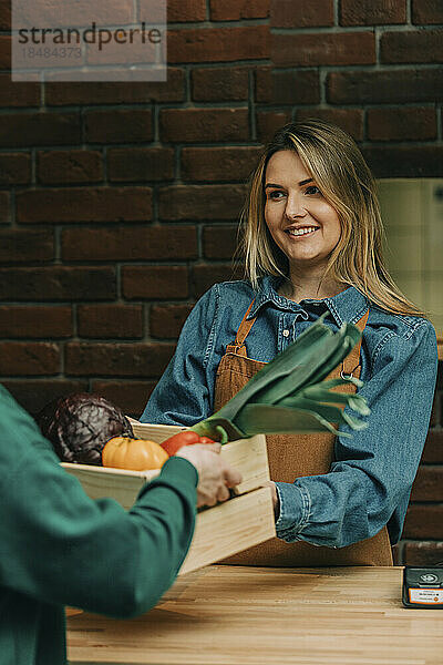 Smiling owner receiving crate of vegetables from delivery person at cafe