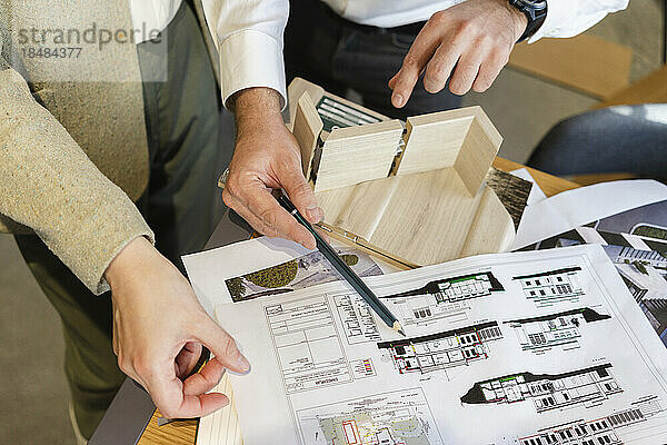 Close-up of two colleagues working on blueprint in architect's office together