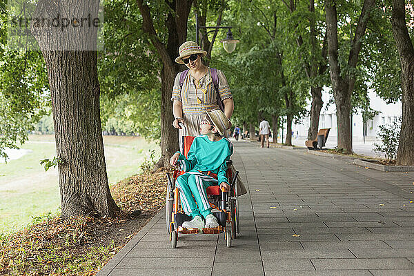 Mutter geht mit Tochter im Rollstuhl auf Gehweg