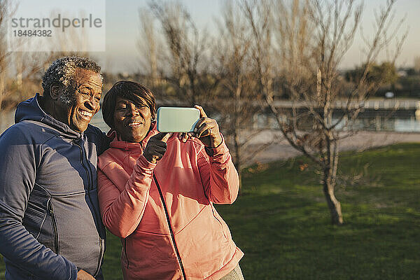 Glückliche Seniorin teilt Smartphone mit Mann im Park