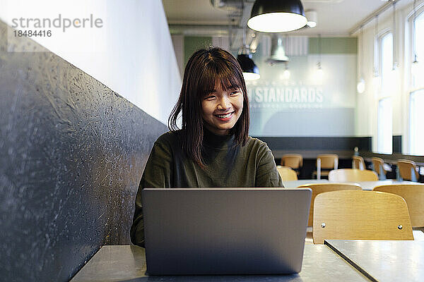 Lächelnde junge Geschäftsfrau mit Laptop-Bürokantine