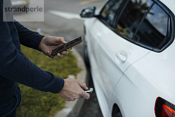 Mann mit Handy schließt Auto mit Schlüssel ab