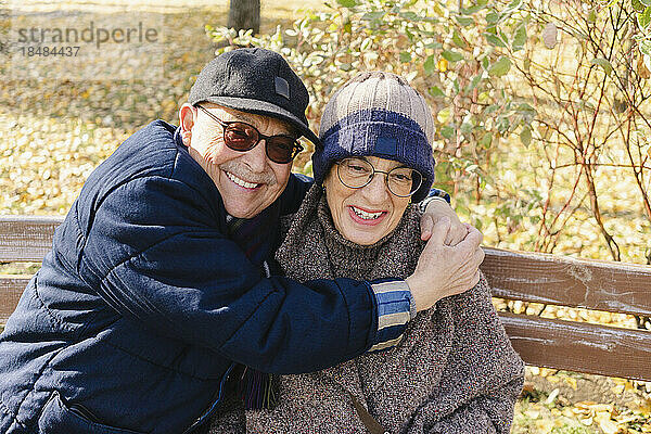 Glücklicher älterer Mann umarmt Frau  die auf Bank sitzt