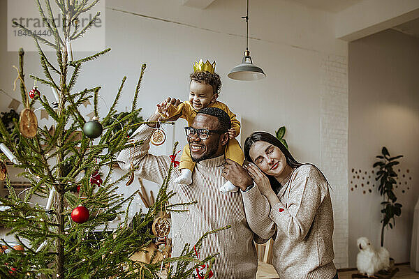 Glücklicher Vater und Mutter mit Tochter  die zu Hause Weihnachtsschmuck berühren