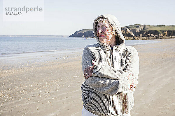 Nachdenkliche ältere Frau mit verschränkten Armen am Strand