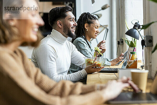 Lächelnder Geschäftsmann beim Mittagessen mit Kollegen im Büro