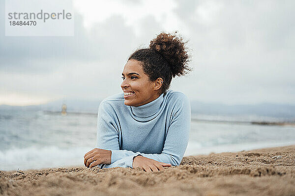 Glückliche junge Frau  die am Strand im Sand liegt