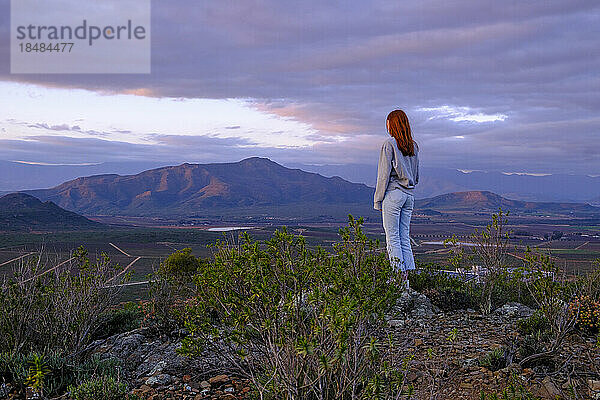 Junge Frau steht bei Sonnenuntergang auf einem Felsen