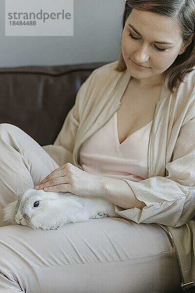 Frau streichelt zu Hause Kaninchen auf dem Schoß