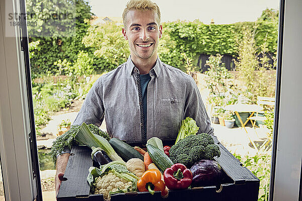 Lächelnder junger Mann hält eine Schachtel Bio-Gemüse in der Hand