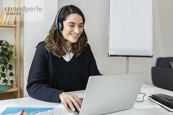 Glückliche Geschäftsfrau mit Headset und Laptop im Büro