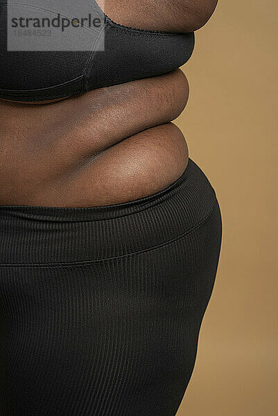Nahaufnahme der Bauch- und Rückenrollen einer Frau in Übergröße vor beigem Hintergrund