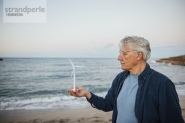 Älterer Mann steht mit Windturbinenmodell vor dem Meer