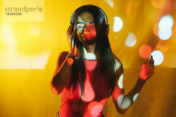 Junge Frau hört Musik über Kopfhörer vor farbigem Hintergrund