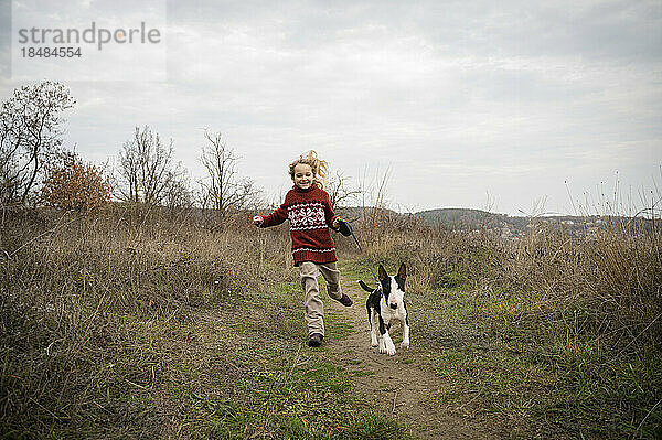 Lächelndes Mädchen läuft mit Hund durch Gras