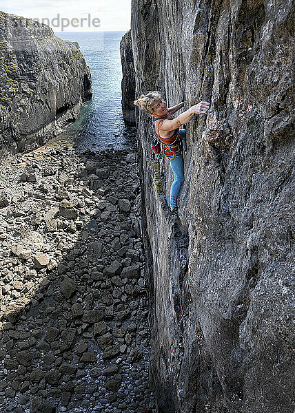 Entschlossene reife Frau klettert an einer Felswand
