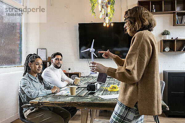 Geschäftsfrau zeigt Kollegen im Büro das Modell einer Windkraftanlage