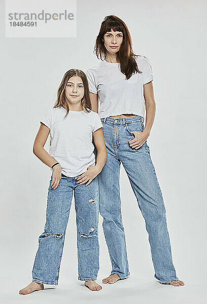 Confident mother and daughter standing against white background