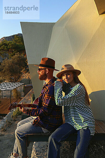 Hipster-Paar sitzt bei Sonnenuntergang zusammen in der Nähe eines Öko-Hauses
