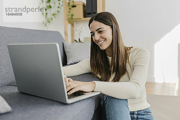 Glückliche junge Frau  die zu Hause auf dem Sofa einen Laptop benutzt