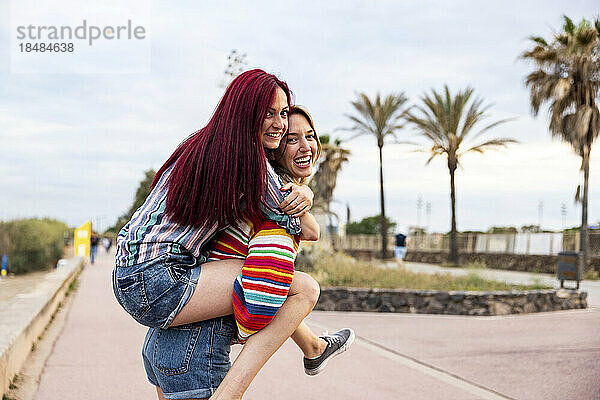 Happy woman giving piggy back ride to friend at promenade