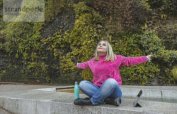 Sorglose reife Frau in rosa Pullover sitzt mit ausgestreckten Armen am Tablet-PC