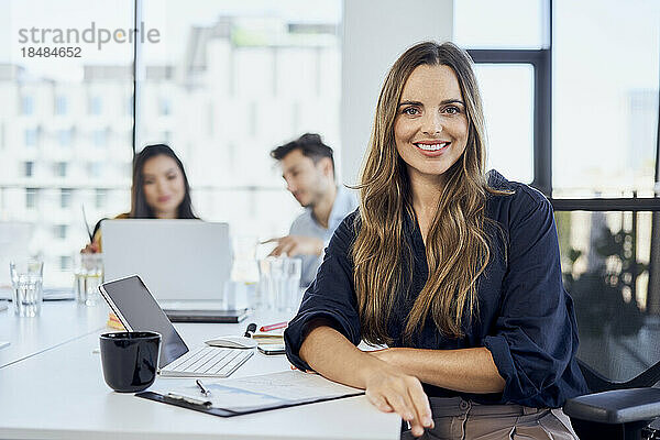 Lächelnde Geschäftsfrau mit Kollegen im Hintergrund im Büro