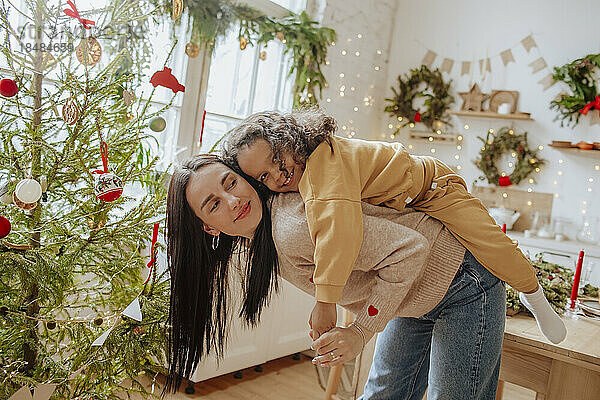 Glückliche Mutter gibt ihrer Tochter zu Weihnachten Huckepackfahrt