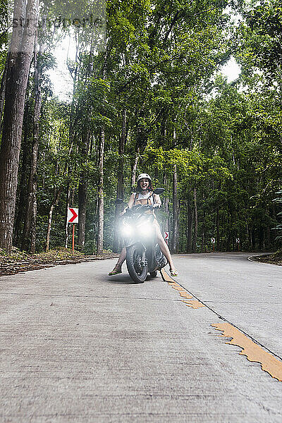 Glückliche Frau sitzt auf Motorrad vor Baum