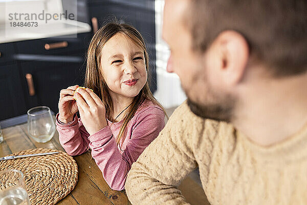 Lächelndes Mädchen beim Frühstück  während der Vater am Tisch sitzt