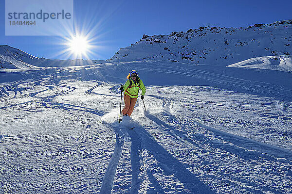 Österreich  Tirol  Die Sonne scheint über einer Skifahrerin  die den schneebedeckten Hang in den Tuxer Alpen hinunterrutscht